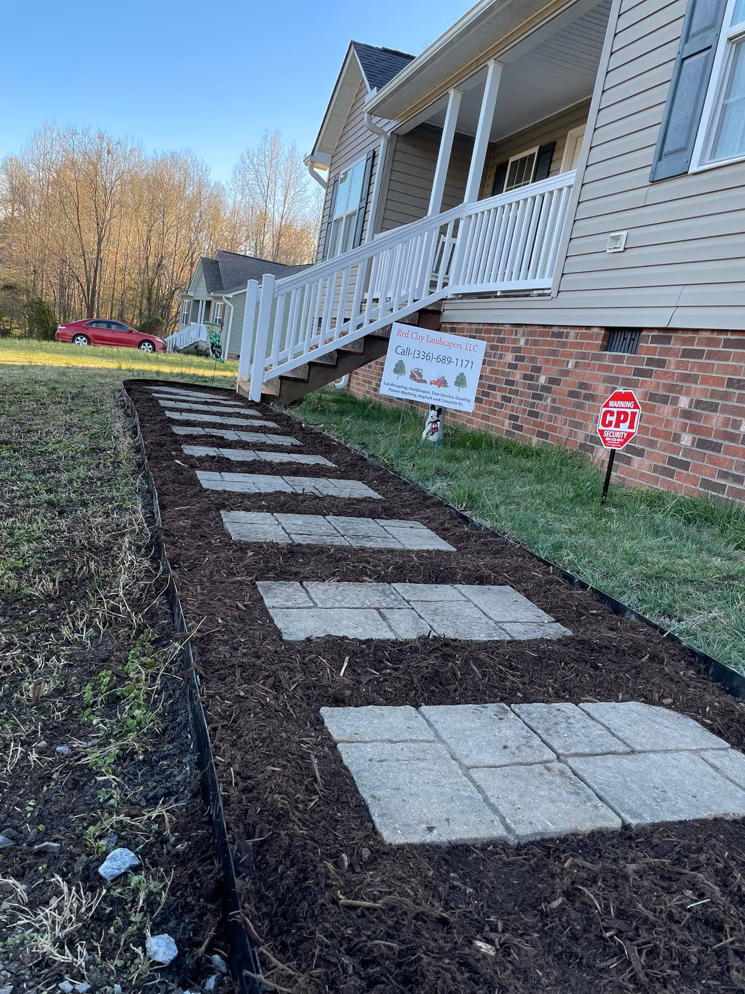 Newly installed pathway of square pavers set in dark mulch leading to house steps with white railing.